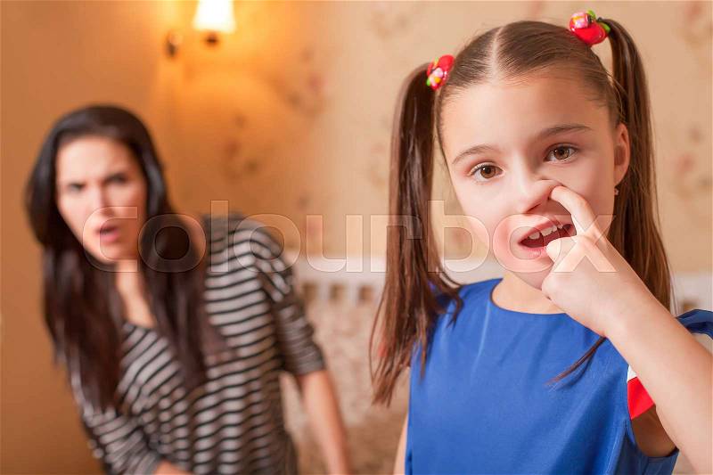 Curious girl picking a nose against surprised mother on the background, stock photo
