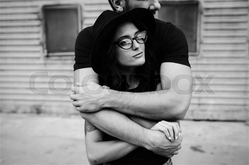 Guy hugging his girlfriend from behind against a background of gray wall, stock photo
