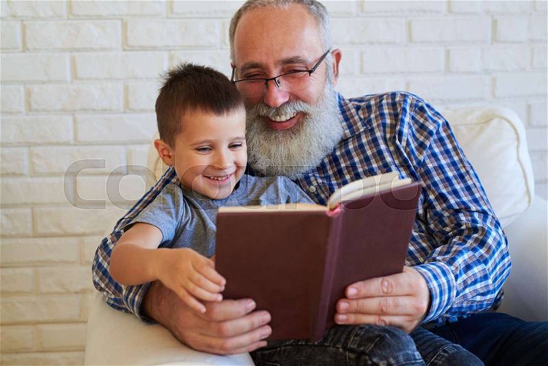 Mid shot of grandson who enjoys reading a book with his granfather. Two book lovers are radiant with the joyful emotions. Concept of education and upbringing, stock photo