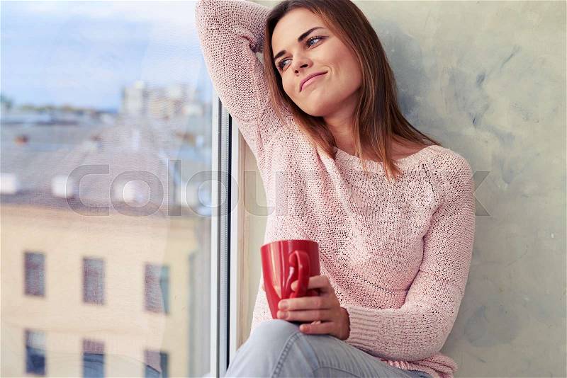 Close-up portrait of carefree youth sitting on the windowsill. Stretches her neck and enjoying a cup of tea in the morning , stock photo