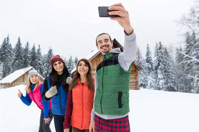 People Group Taking Selfie Photo On Smart Phone Near Wooden Country House Winter Snow Mountain Resort Cottage Friends On Vacation, stock photo