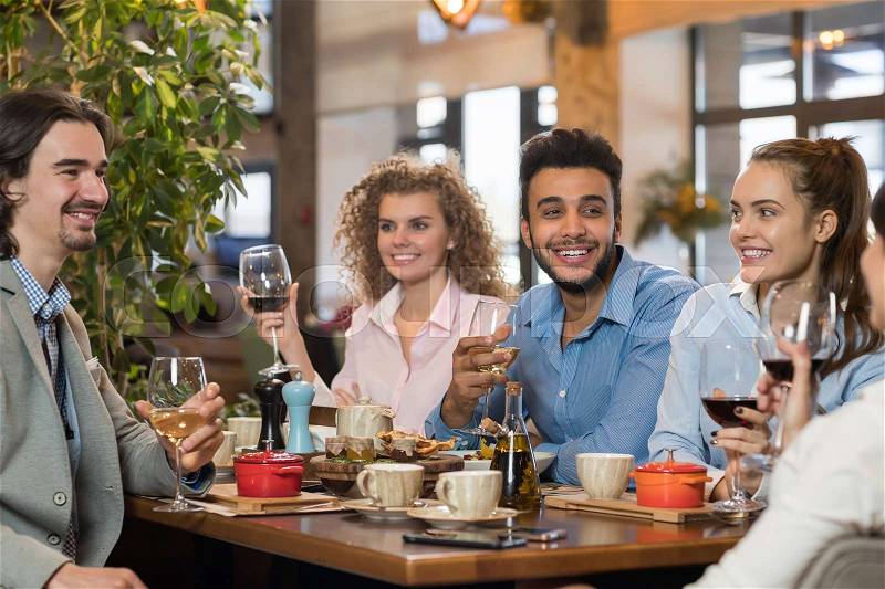 Young Business People Group Drink Wine Sitting Restaurant Table, Friends Hold Glasses Toasting Smiling Mix Race Men Women, stock photo