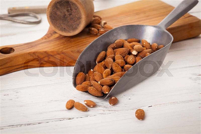 Peeled almonds on tin shovel, kitchen utensils in background, stock photo