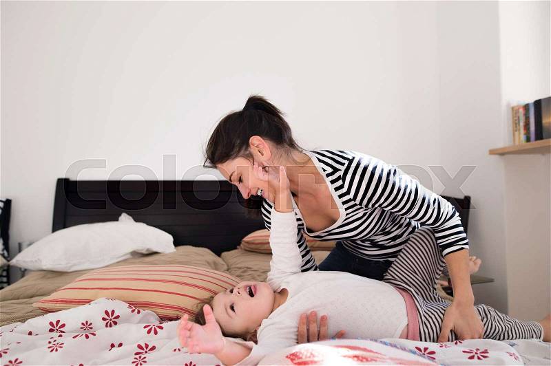Beautiful young mother with her cute little daughter lying on bed, having fun, stock photo
