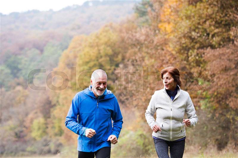 Beautiful active senior couple running together outside in sunny autumn nature, stock photo