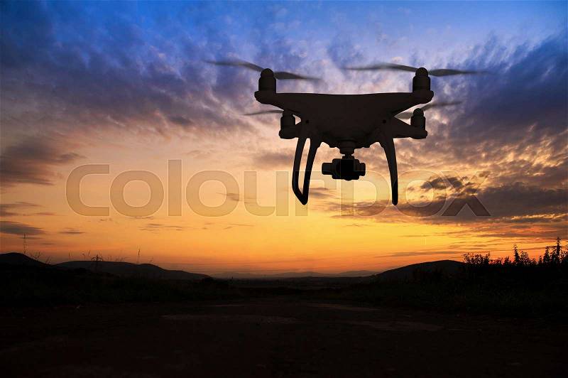 Silhouette of hovering drone taking pictures of green meadows and hills at sunset, stock photo