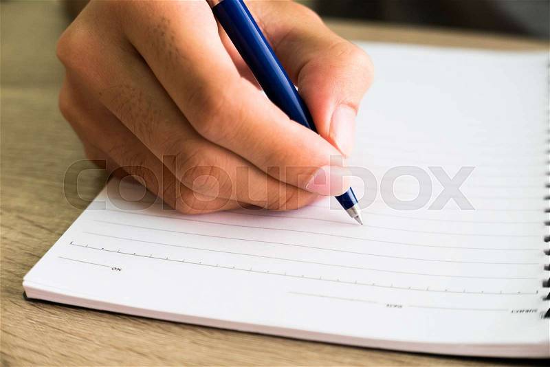 Closeup of male right hand writing text on blank notebook on wooden desk in office, stock photo
