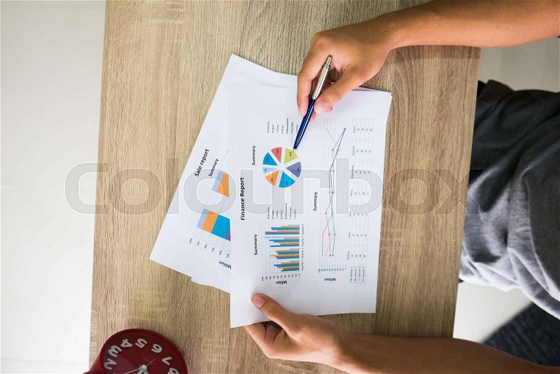 Closeup of male right hand holding pen points on colorful business graph in office top view, stock photo