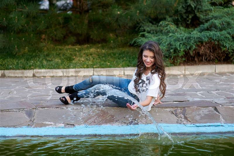 Beautiful woman sitting near the fountain in the Park, stock photo