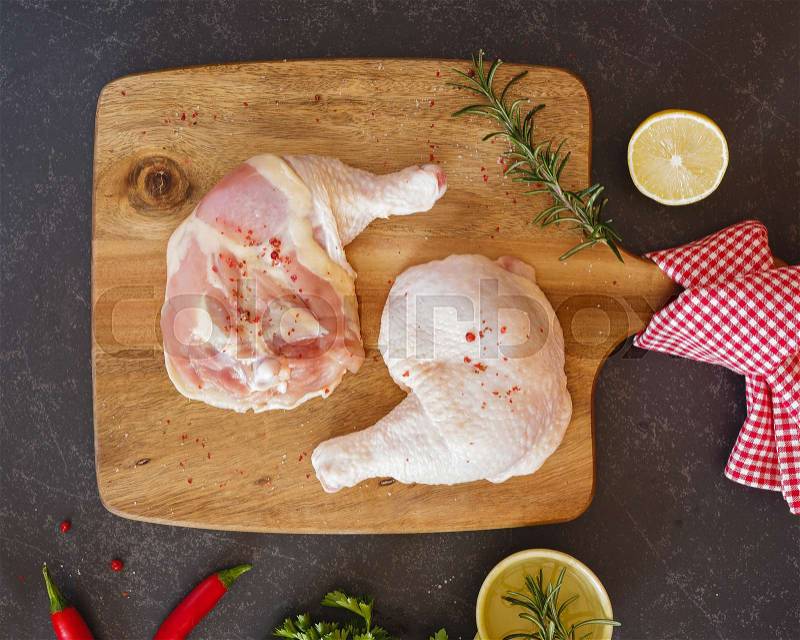 Fresh and raw chicken legs and thighs on a chopping board with various fresh herbs and spices on dark background, top view, stock photo