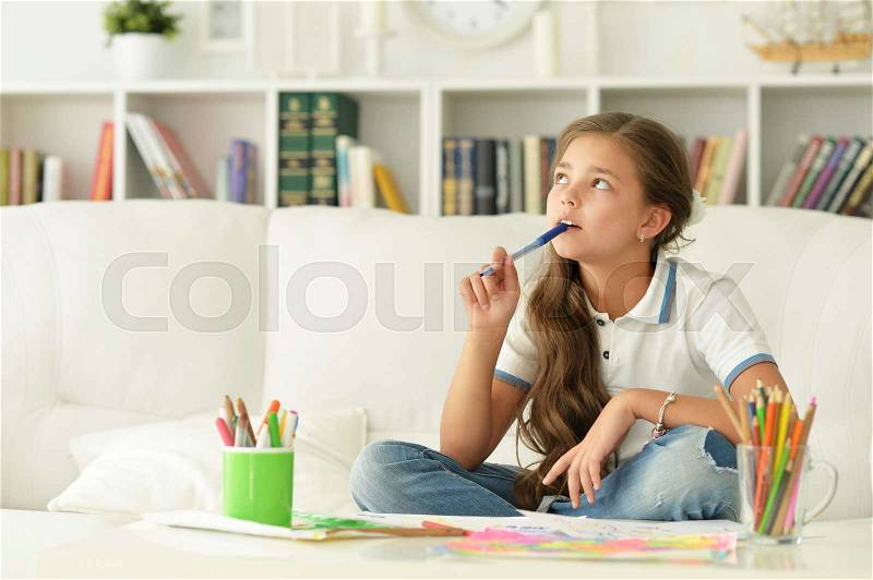 Little girl drawing with pencils sitting on sofa at home, stock photo