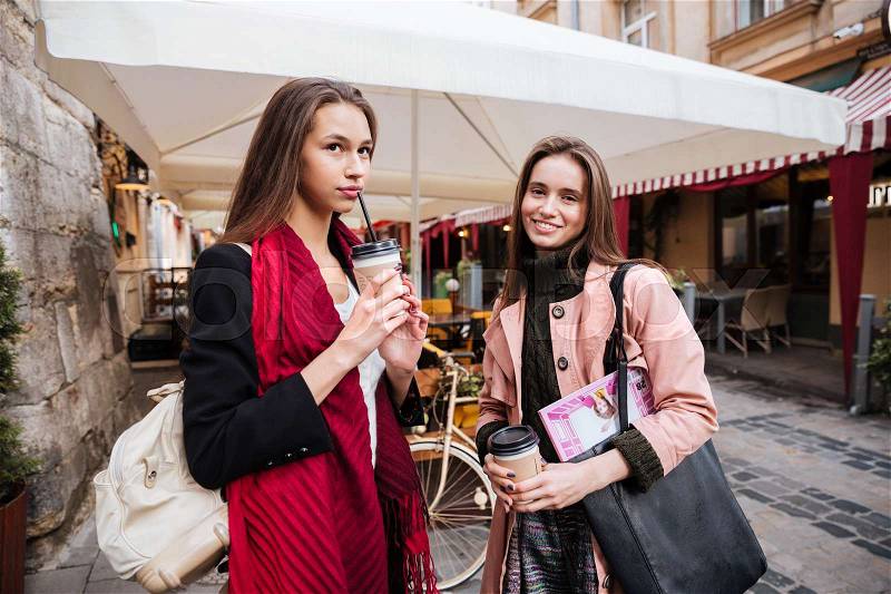 Two fashion models in coats on the street. smiling. drink coffee, stock photo