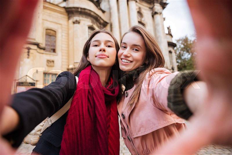 Girls in coats makes selfie. grimace. on the street, stock photo