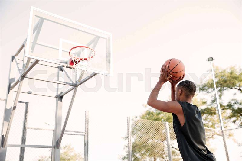 Photo of young african basketball player practicing in the street with trees on background, stock photo