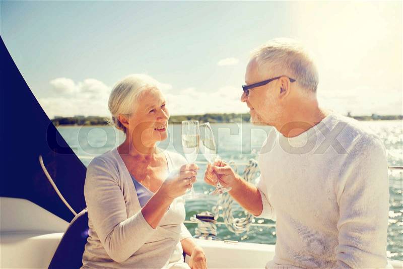 Sailing, age, travel, holidays and people concept - happy senior couple clinking champagne glasses on sail boat or yacht deck floating in sea, stock photo