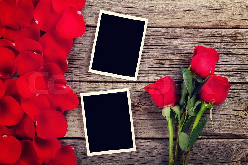 Red roses, photo frames and petals over wooden table. Toned, stock photo