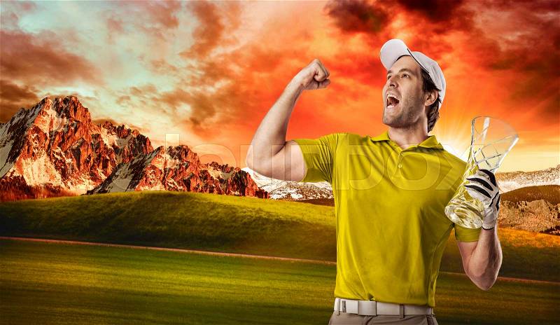 Golf Player in a yellow shirt celebrating with a glass trophy in his hands, on a golf course, stock photo