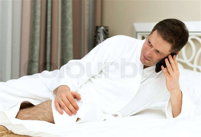 Man in bathrobe using mobile phone in hotel room, stock photo