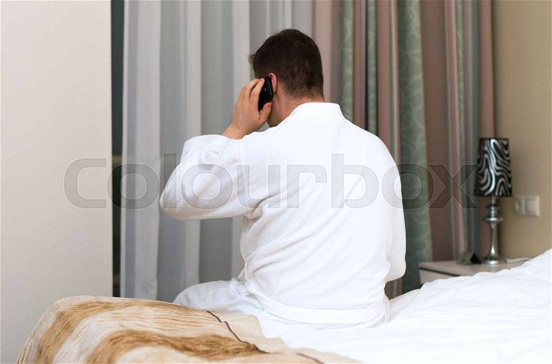 Man in bathrobe with mobile phone in hotel room, stock photo