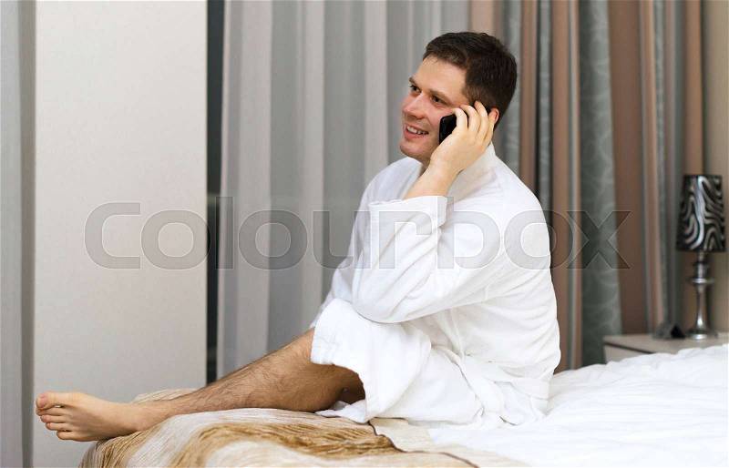Happy man in bathrobe with mobile phone in hotel room, stock photo