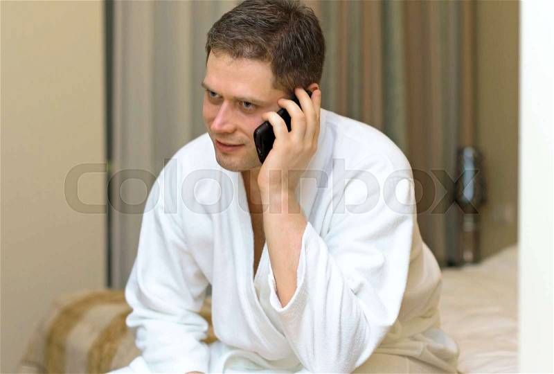 Man in bathrobe with mobile phone in hotel room, stock photo