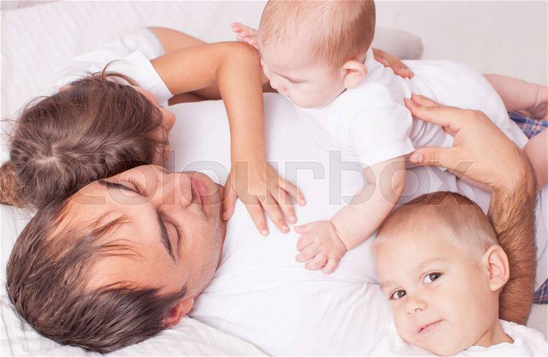 The father with three children in white laughing and playing on the bed, stock photo