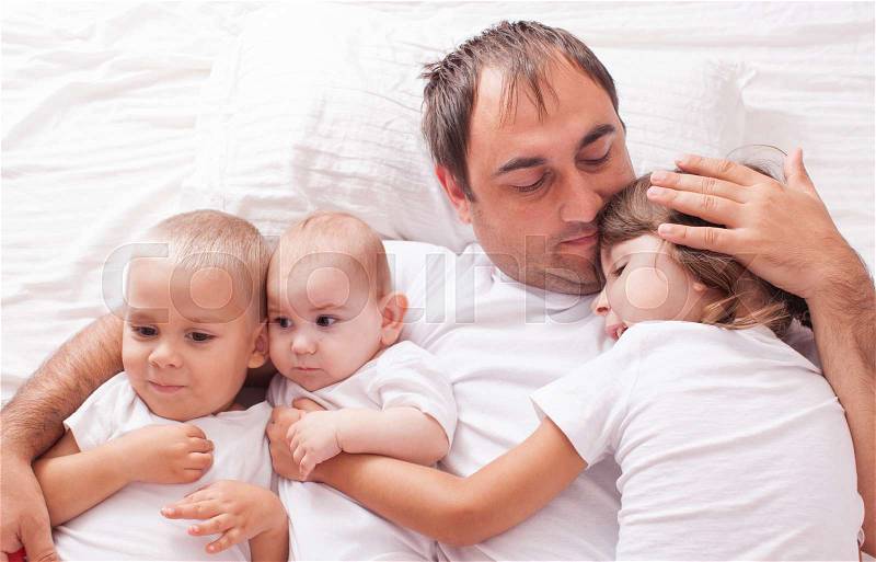 The father with three children in white laughing and playing on the bed, stock photo
