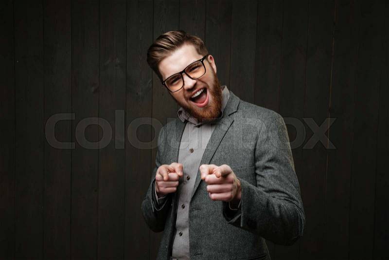 Portrait of an excited bearded man in eyeglasses pointing fingers at camera, stock photo