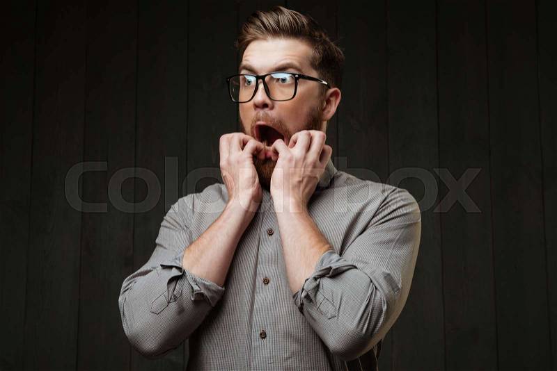 Portrait of a scared bearded man in eyeglasses looking away isolated on the black wooden background, stock photo
