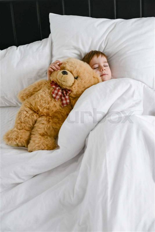 Photo of little cute boy sleeping with teddy bear in bed. Eyes closed, stock photo