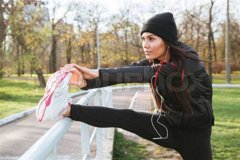Image of fitness lady in warm clothes and headphones in autumn park make sport exercise, stock photo