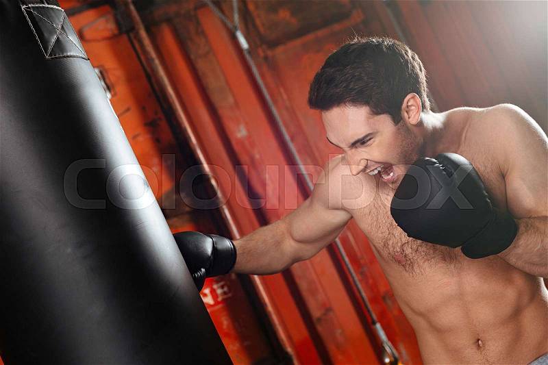 Image of screaming strong boxer training in a gym with punchbag. Looking at punchbag, stock photo