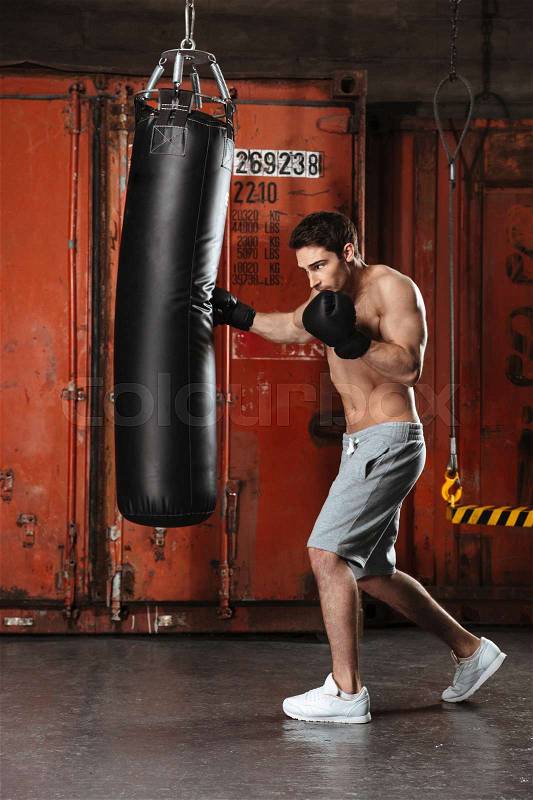 Picture of handsome young boxer training in a gym with punchbag. Looking aside, stock photo