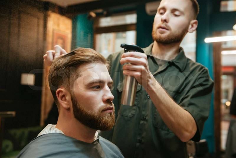 Photo of hipster man getting haircut by hairdresser while sitting in chair, stock photo