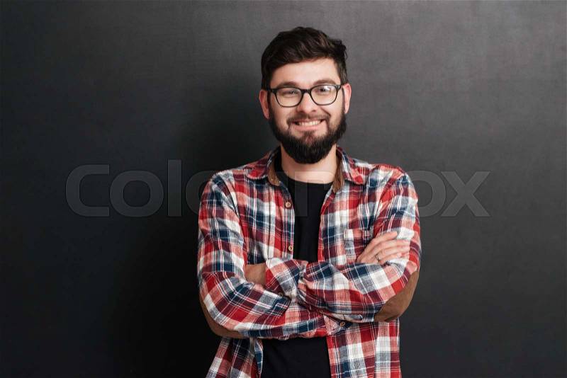 Happy man dressed in shirt in a cage and wearing glasses standing over chalkboard with arms crossed, stock photo