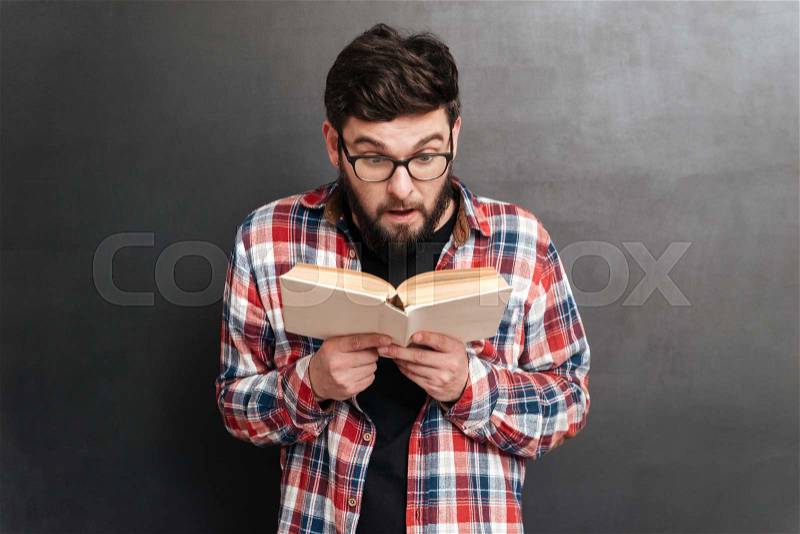 Surprised man dressed in shirt in a cage and wearing glasses standing over chalkboard while reading a book, stock photo
