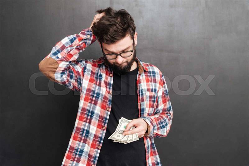 Photo of confused man dressed in shirt in a cage and wearing glasses standing over chalkboard while holding money, stock photo