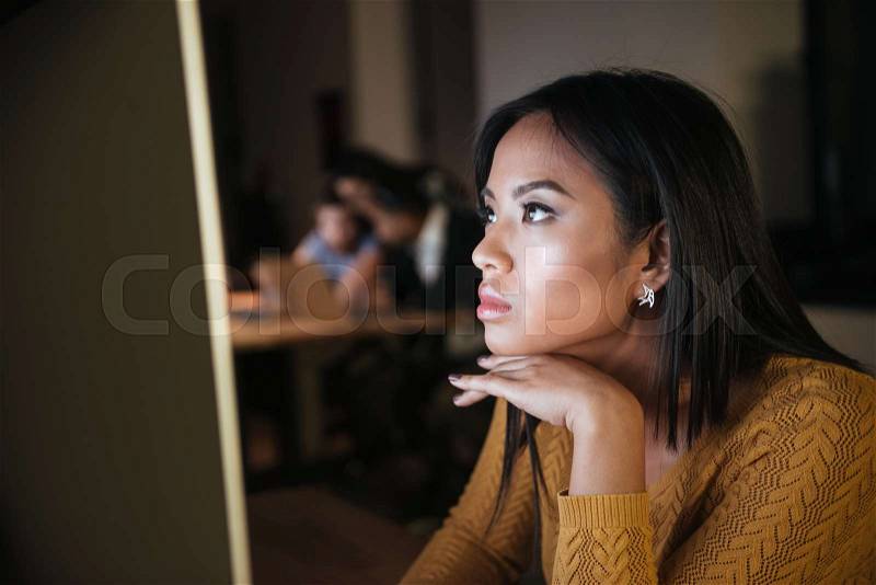 Concentrated african businesswoman working late at night in office with computer. Looking at computer, stock photo