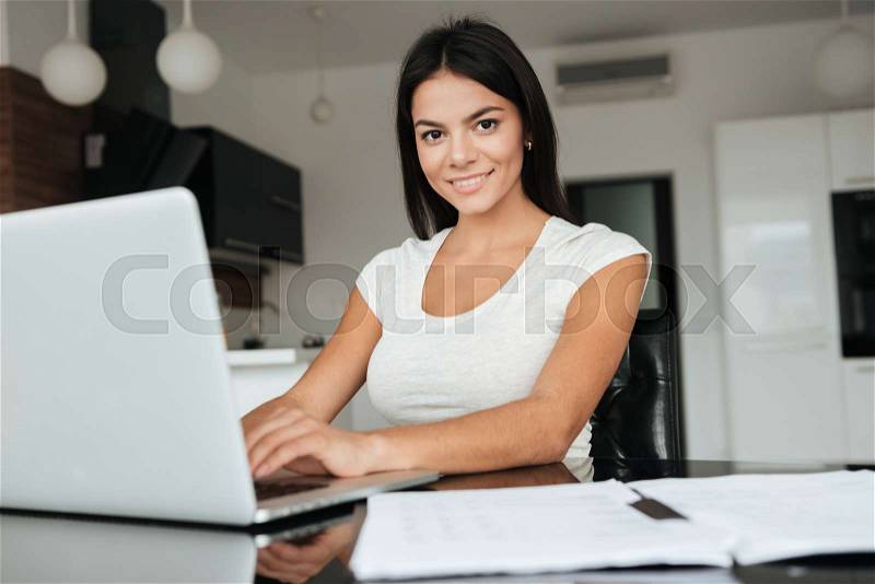 Photo of young woman typing by laptop and analyzing home finances. Look at camera, stock photo