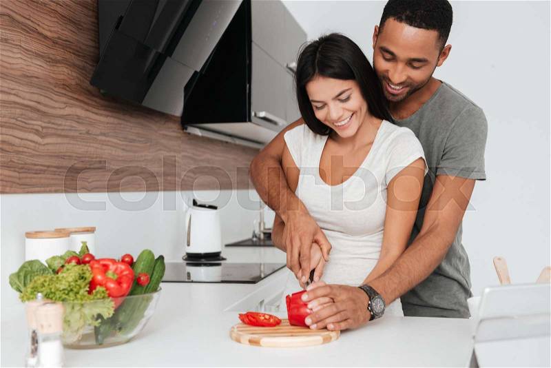 Picture of cheerful young couple in the kitchen hugging while cooking, stock photo