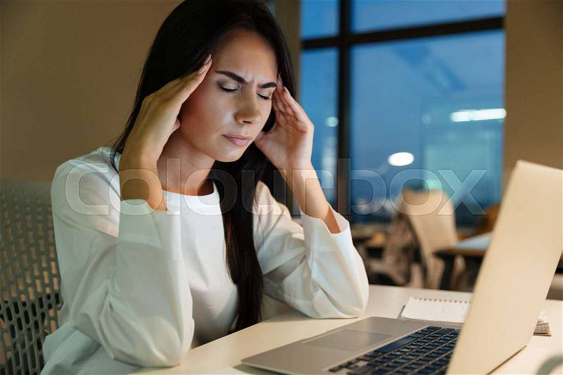 Tired fatigued young businesswoman touching her temples and having headache in office, stock photo