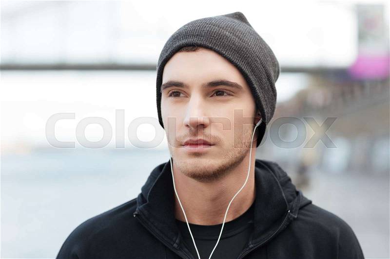 Portrait of attractive young man in hat listening to music with earphones outdoors, stock photo