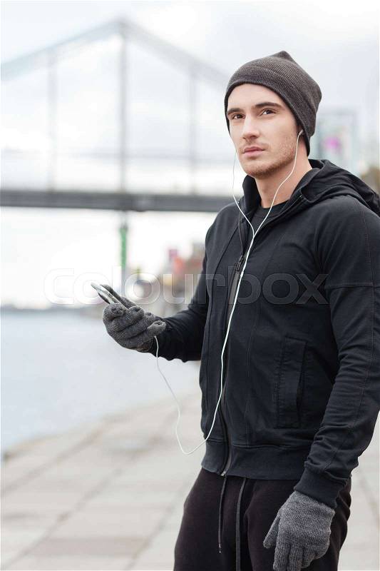Pensive young man thinking and listening to music from cell phone outdoors, stock photo