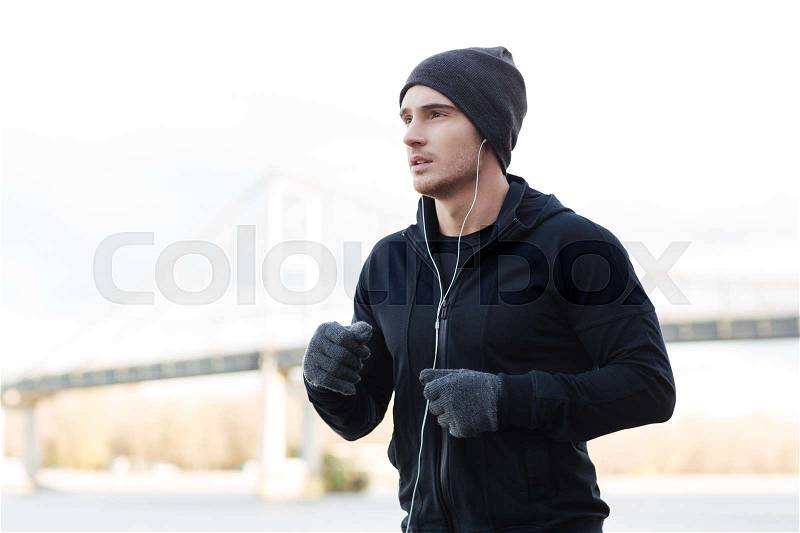 Attractive young man athlete in earphones listening to music and running outdoors, stock photo