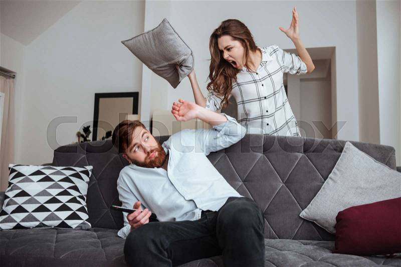 Photo of angry young lady screaming to man while he sitting at sofa, stock photo