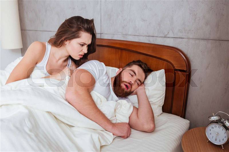 Photo of young angry woman looking at her boyfriend while he sleeping, stock photo