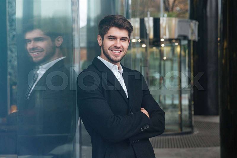 Photo of young happy businessman dressed in official clothing standing near business center and look at camera, stock photo