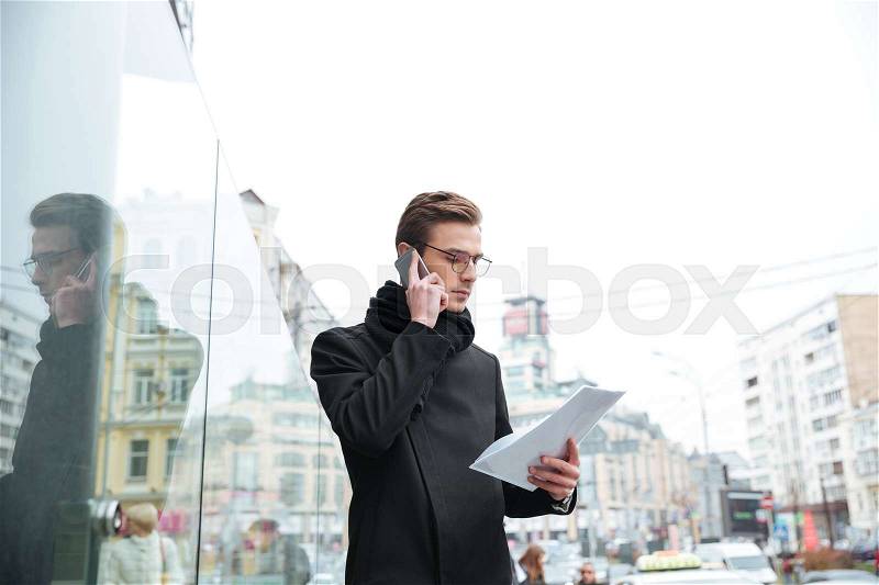 Side view of serious business man with phone and documents on the street, stock photo
