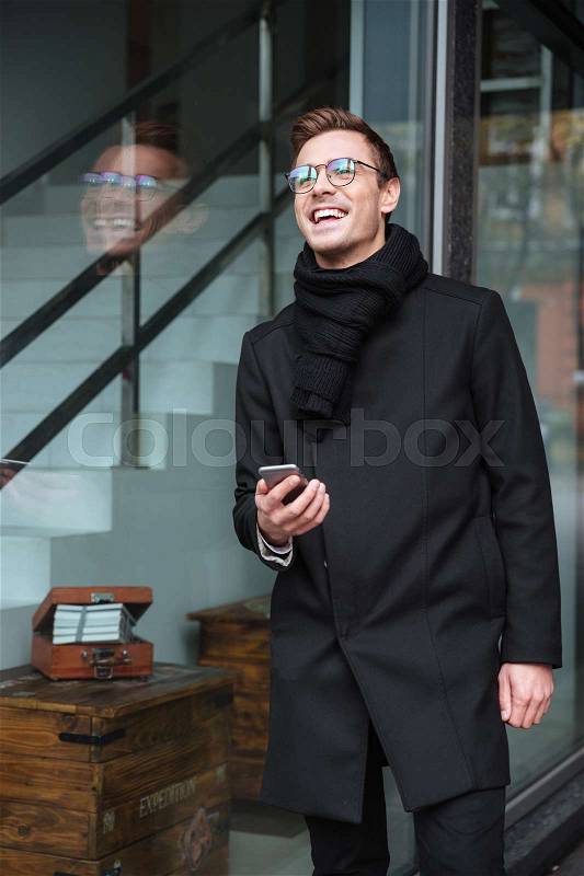 Vertical image of business man in glasses with phone near the building, stock photo