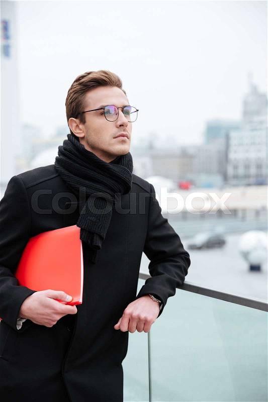 Vertical image of business man in glasses and warm clothes with folder outdoors, stock photo